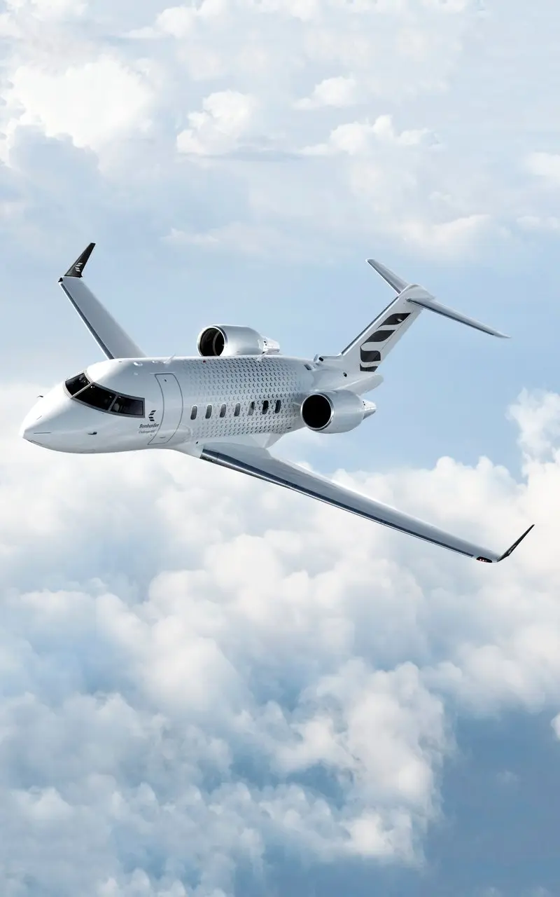 The Bombardier Challenger 650 private jet is seen flying above white clouds, showcasing its sleek exterior design from a side view.