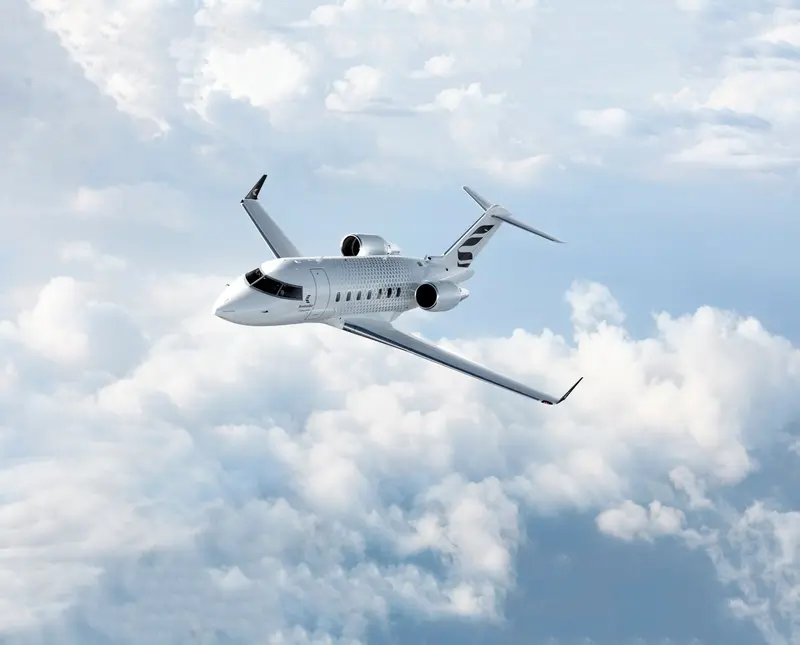 Bombardier Challenger 650 – Private jet in flight The Bombardier Challenger 650 private jet is seen flying above white clouds, showcasing its sleek exterior design from a side view.
