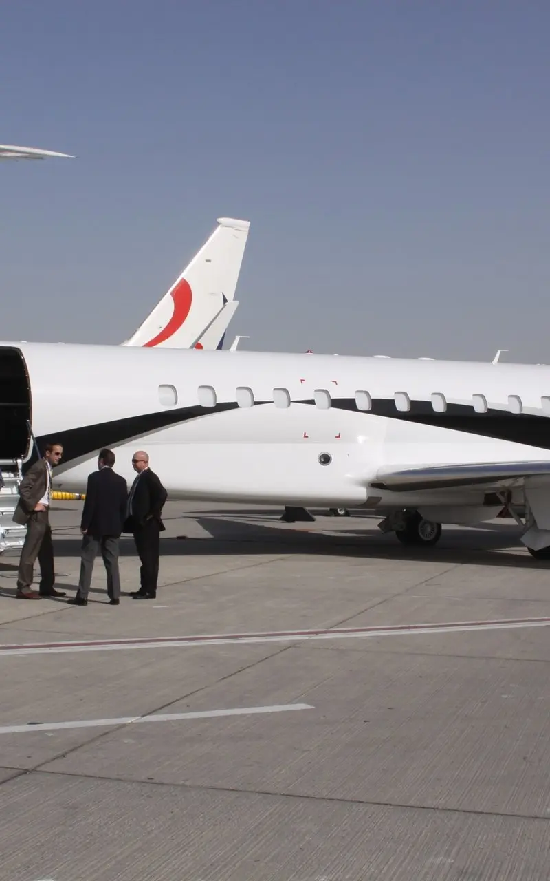 Embraer Legacy 650 — Side view on airfield The Embraer Legacy 650 private jet is seen from the side on an airfield in Ibiza, with its main door open and three men standing nearby.