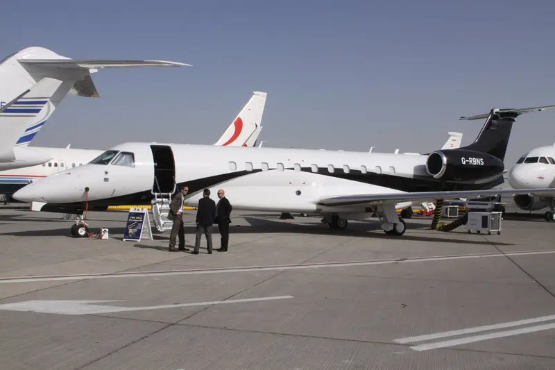 Embraer Legacy 650 — Side view on airfield The Embraer Legacy 650 private jet is seen from the side on an airfield in Ibiza, with its main door open and three men standing nearby.