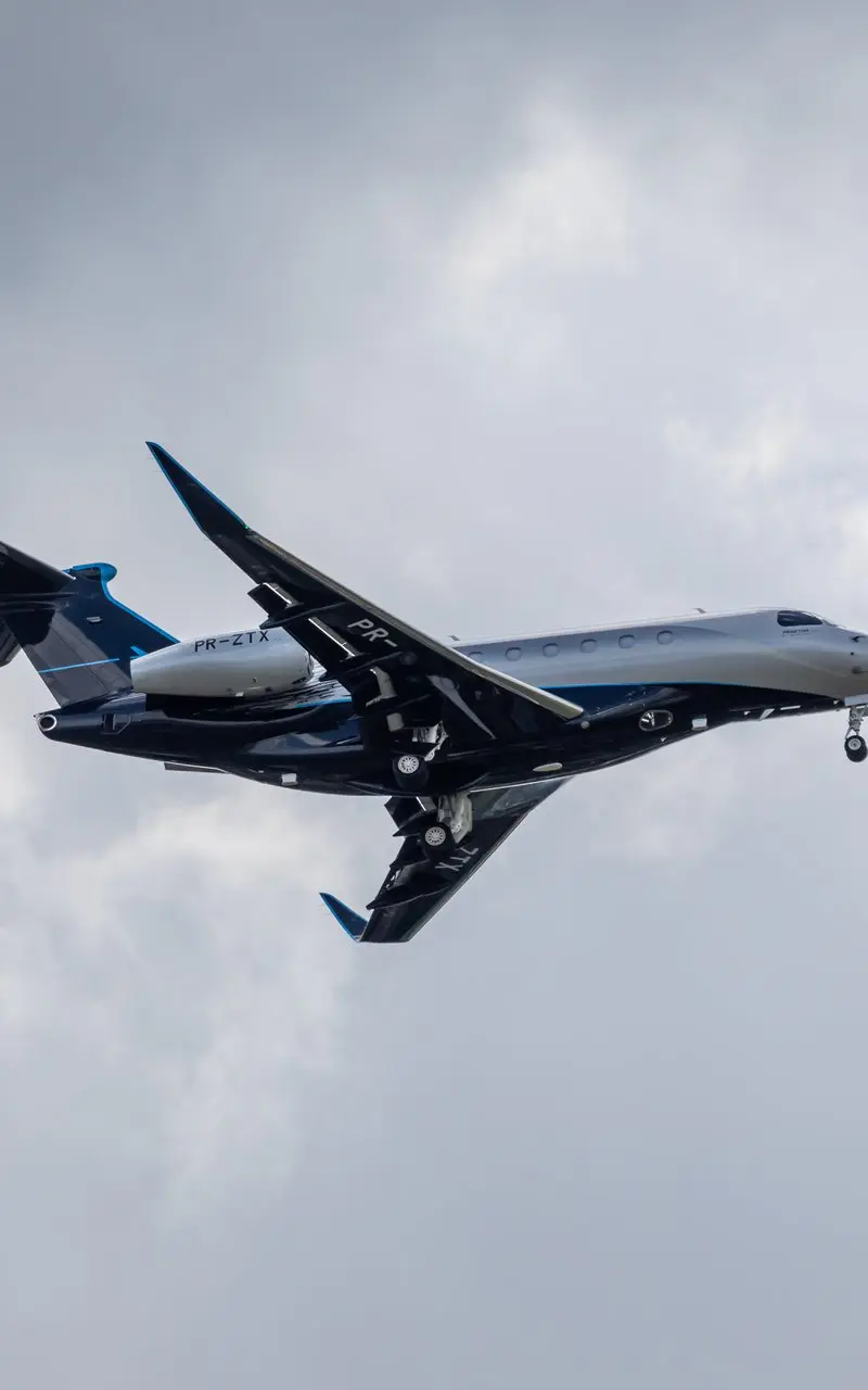 Embraer Praetor 600 — In flight over Barcelona The sleek Embraer Praetor 600 private jet is captured in flight with its landing gear deployed against a cloudy sky over Barcelona.