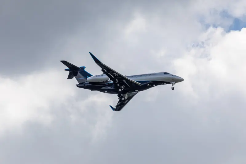 Embraer Praetor 600 — In flight over Barcelona The sleek Embraer Praetor 600 private jet is captured in flight with its landing gear deployed against a cloudy sky over Barcelona.