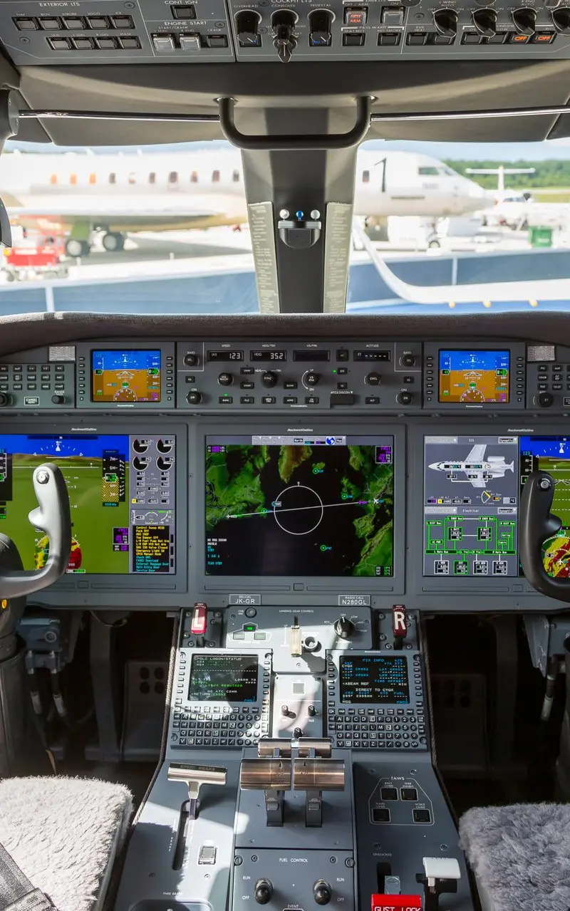 Gulfstream G280 — Advanced cockpit view The advanced cockpit of a Gulfstream G280 private jet, featuring multiple digital displays, flight controls, and a view of other aircraft on the tarmac.