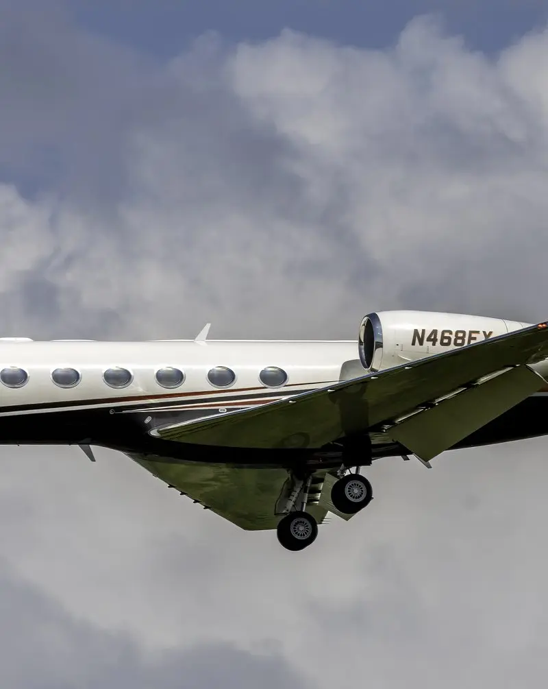 Gulfstream G450 — Private jet in flight over Madrid A white and black Gulfstream G450 private jet in flight with its landing gear extended, seen from the side against a cloudy sky over Madrid.