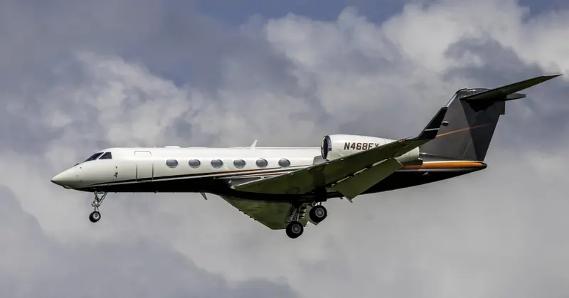 Gulfstream G450 — Private jet in flight over Madrid A white and black Gulfstream G450 private jet in flight with its landing gear extended, seen from the side against a cloudy sky over Madrid.