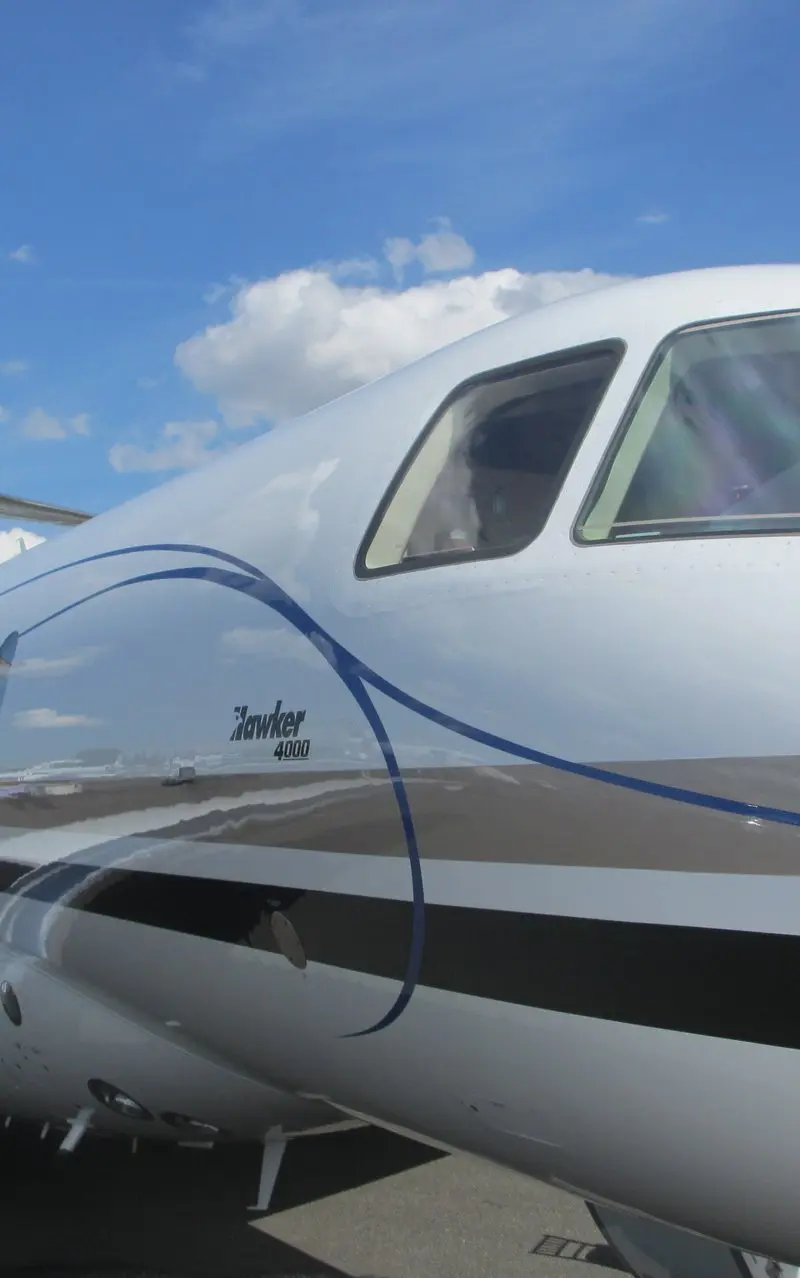 Hawker 4000 – Front fuselage and cockpit in Madrid Hawker 4000 private jet's front-side fuselage, cockpit windows, and engine under a blue sky, ready for routes from Madrid.
