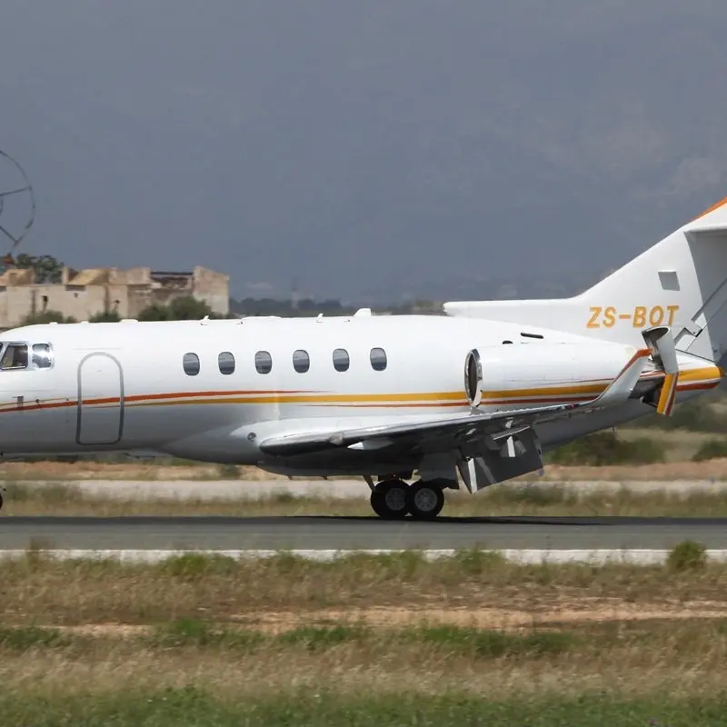 Hawker 900XP — Luxury private jet on Malaga runway The Hawker 900XP private jet is seen from the side, taxiing on a runway in Malaga with historical buildings in the background.