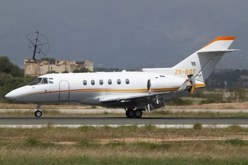 Hawker 900XP — Luxury private jet on Malaga runway The Hawker 900XP private jet is seen from the side, taxiing on a runway in Malaga with historical buildings in the background.