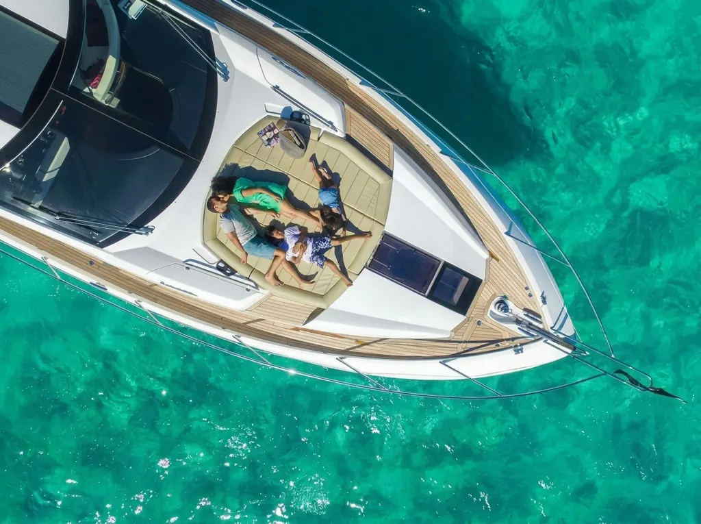 Sunseeker 68 Sport Yacht — Family on bow sunpad An aerial view shows a family relaxing on the Sunseeker 68 Sport Yacht's bow sunpad over turquoise waters in Marbella.